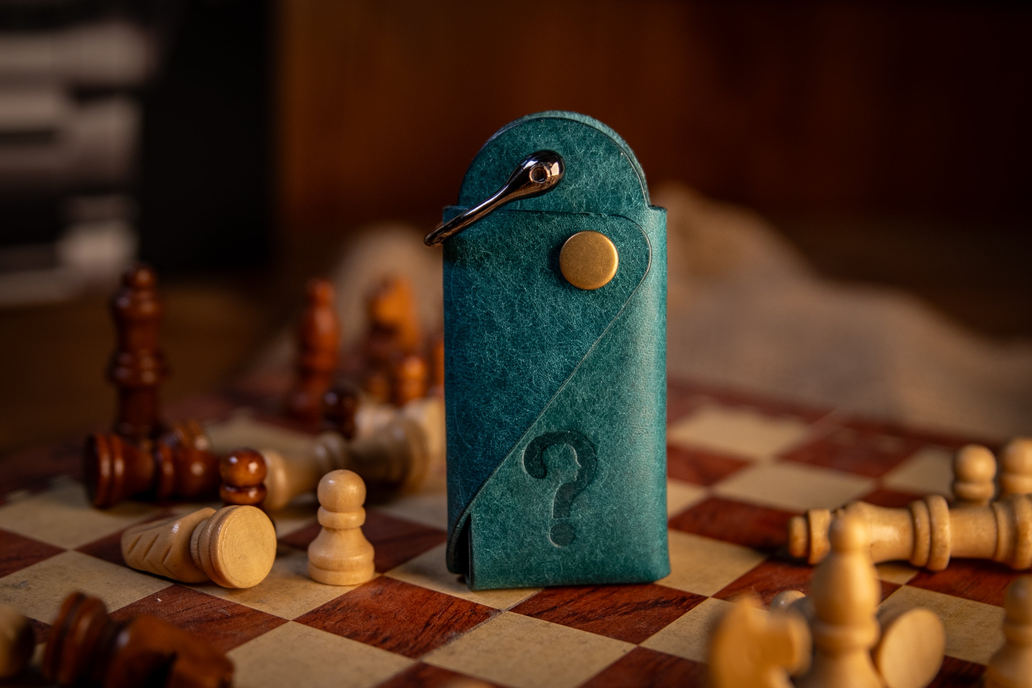 Blue leather key organiser  with a question mark on a chessboard with wooden chess pieces.
