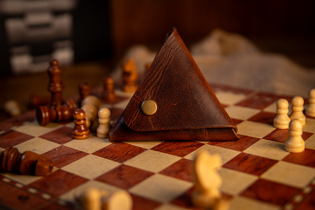 Brown leather triangle-shaped pouch on a chessboard with chess pieces around