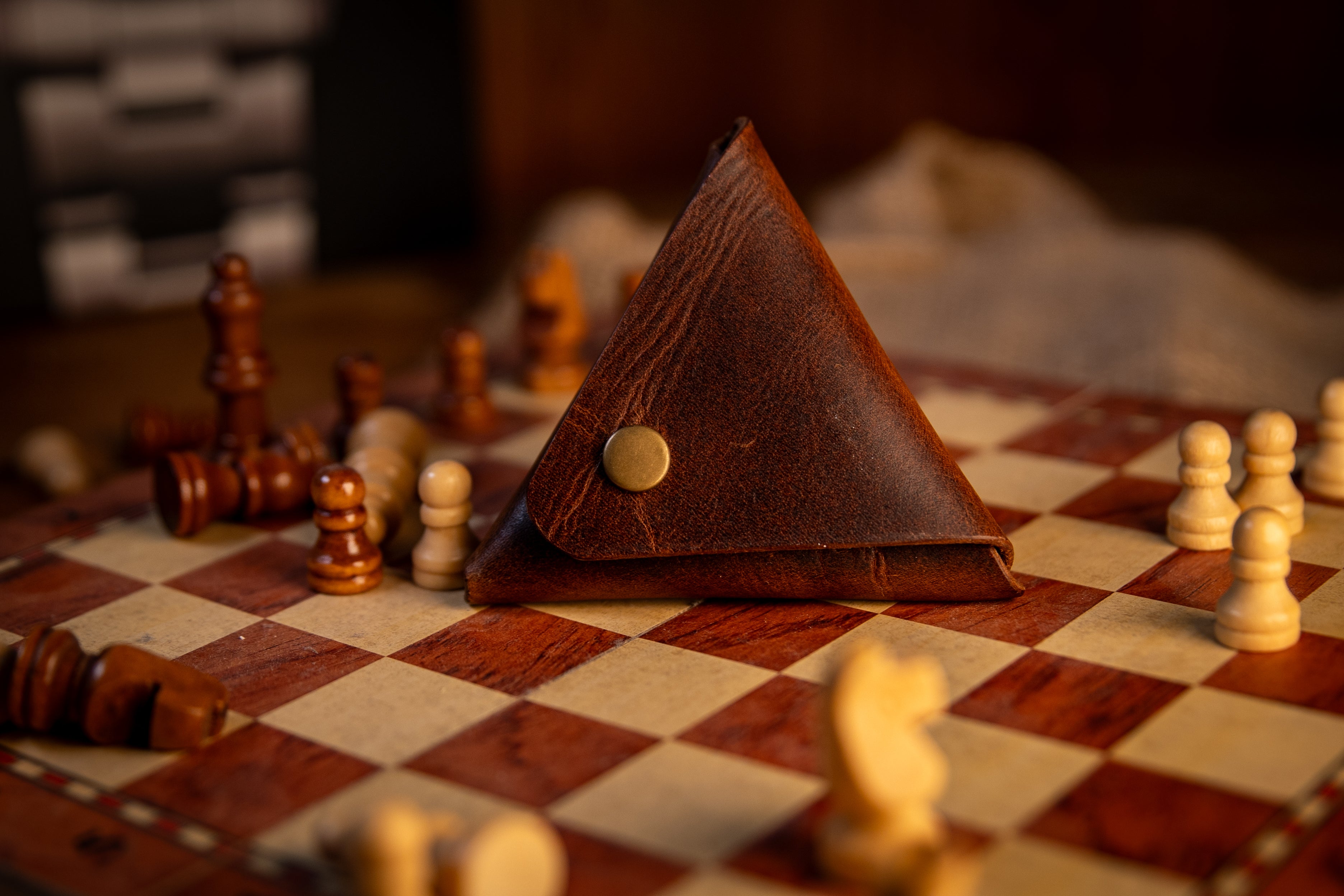Brown leather triangle-shaped pouch on a chessboard with chess pieces around