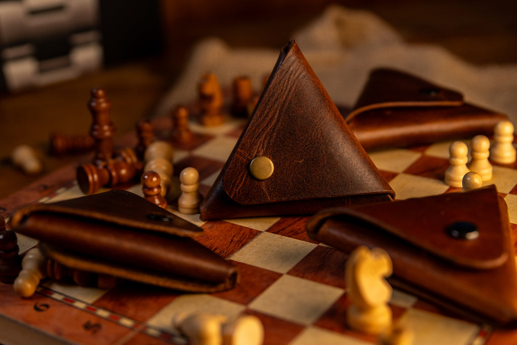 Brown leather triangle-shaped item on a chessboard with chess pieces.