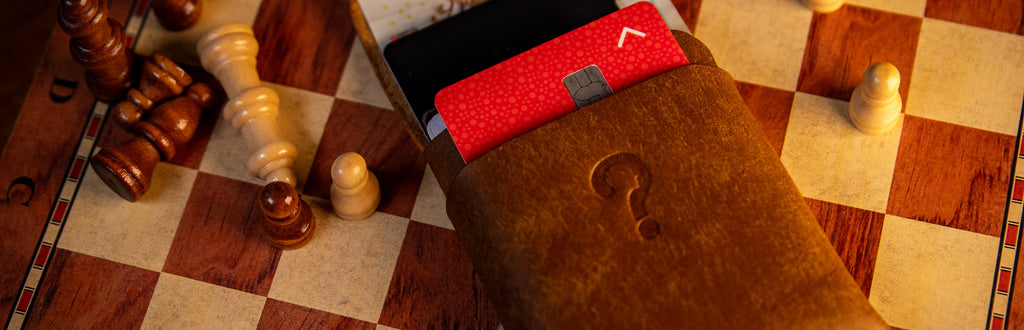 Close-up of a brown  pueblo leather wallet with a red pattern on a checkered wooden surface with chess pieces.