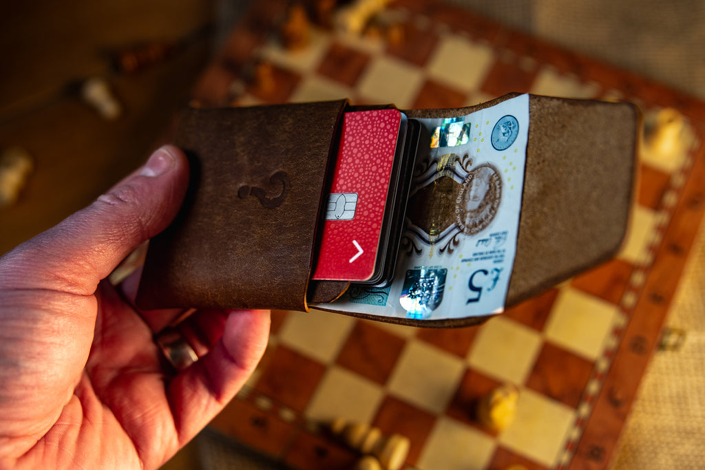 Hand holding a brown pueblo leather wallet with cards on a checkered surface