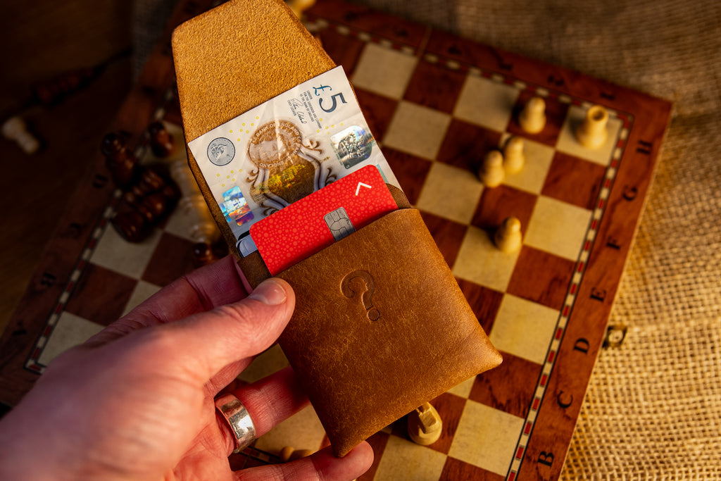Brown pueblo leather wallet with money held over a checkered surface