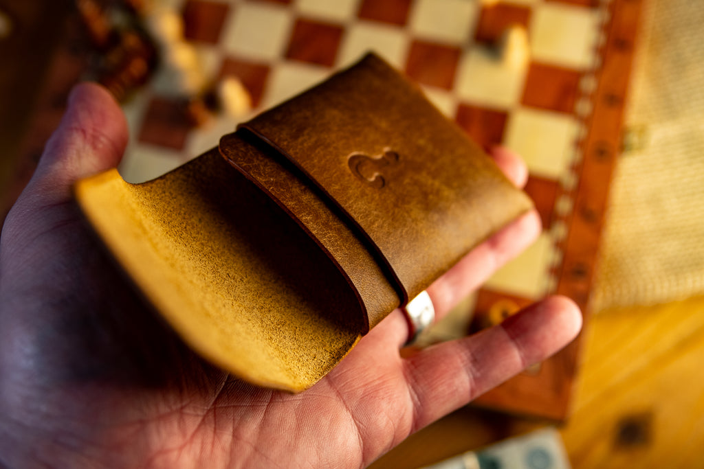 Hand holding a brown pueblo leather wallet with a heart emblem on a checkered tablecloth.