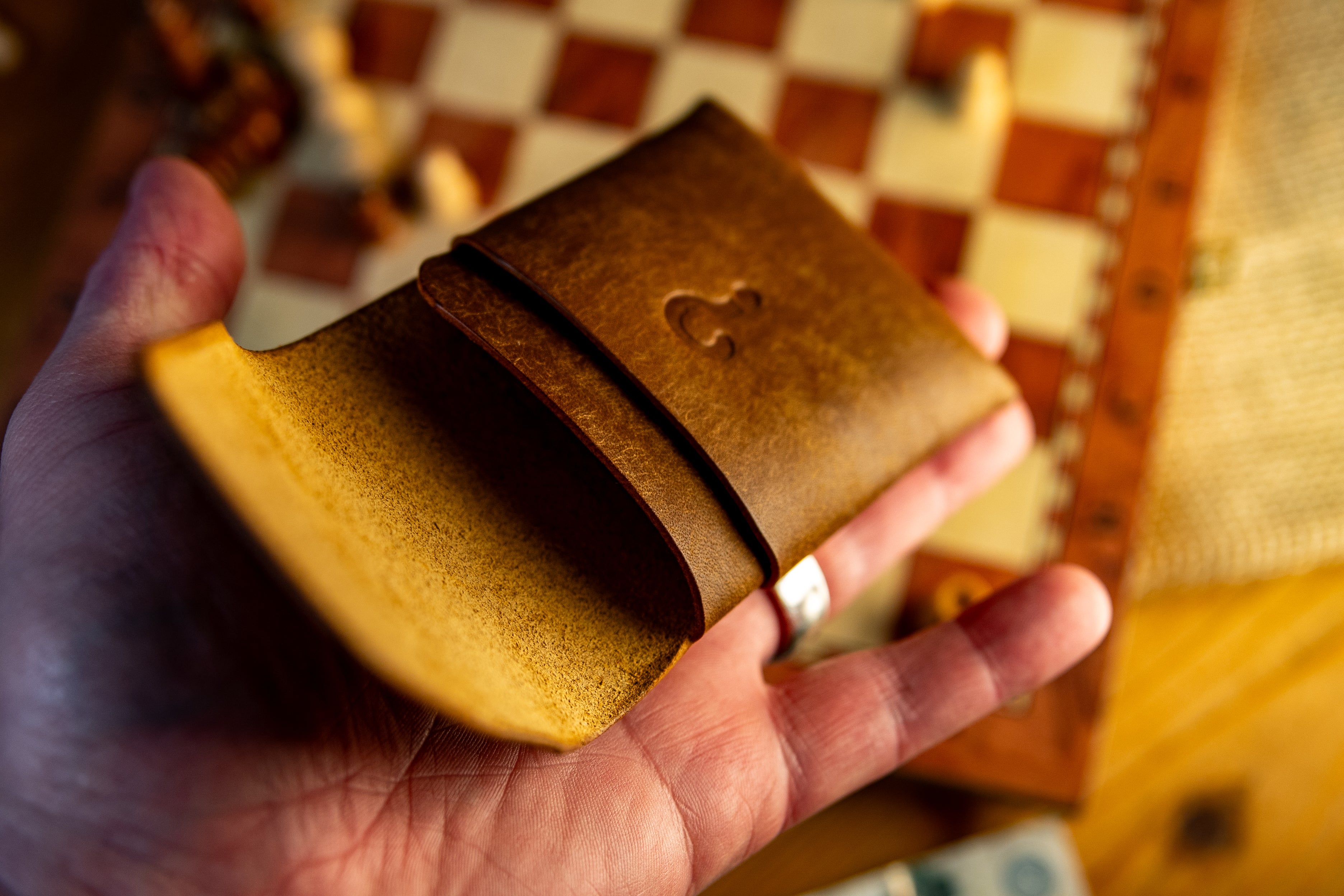 Hand holding a brown pueblo leather wallet with a heart emblem on a checkered tablecloth.