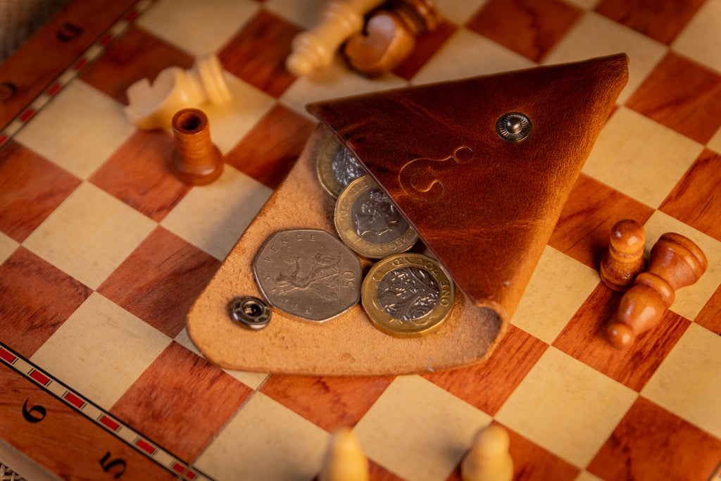 Triangular leather case with coins on a checkered wooden surface