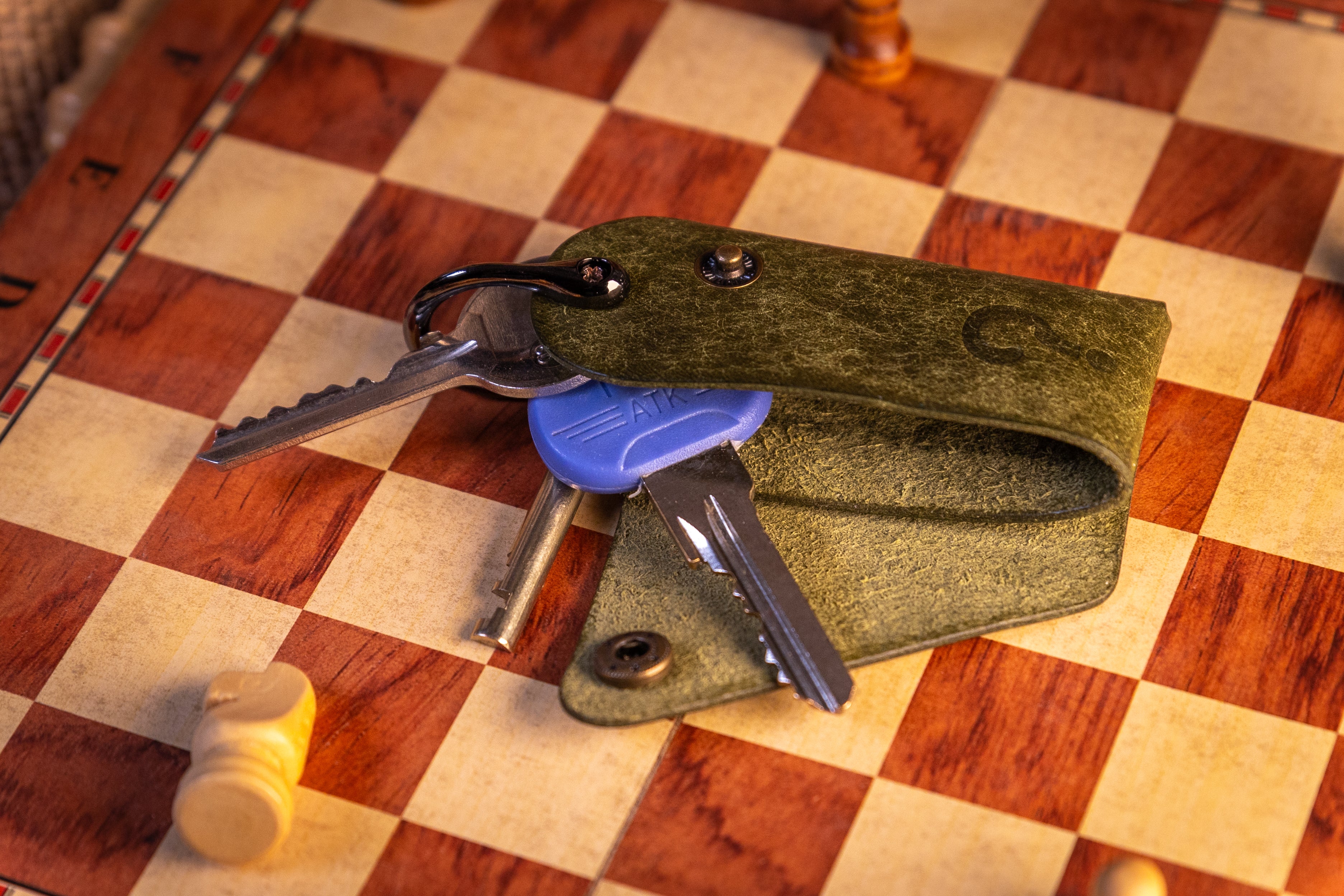 Green leather key organiser with keys on a checkered wooden surface