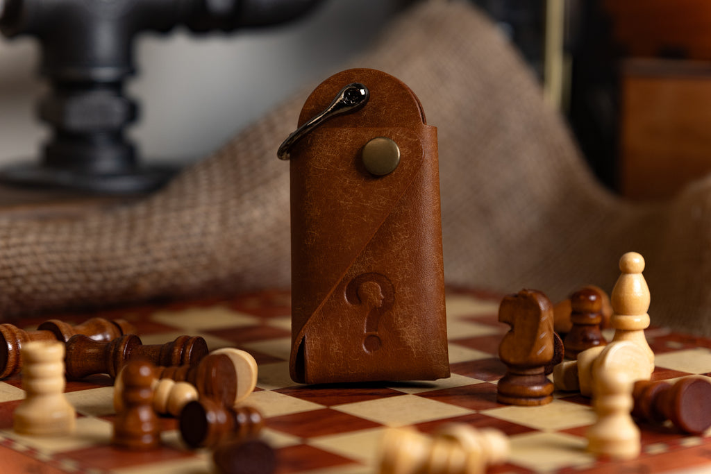 Brown leather case with a metallic clasp on a chessboard with scattered pieces.