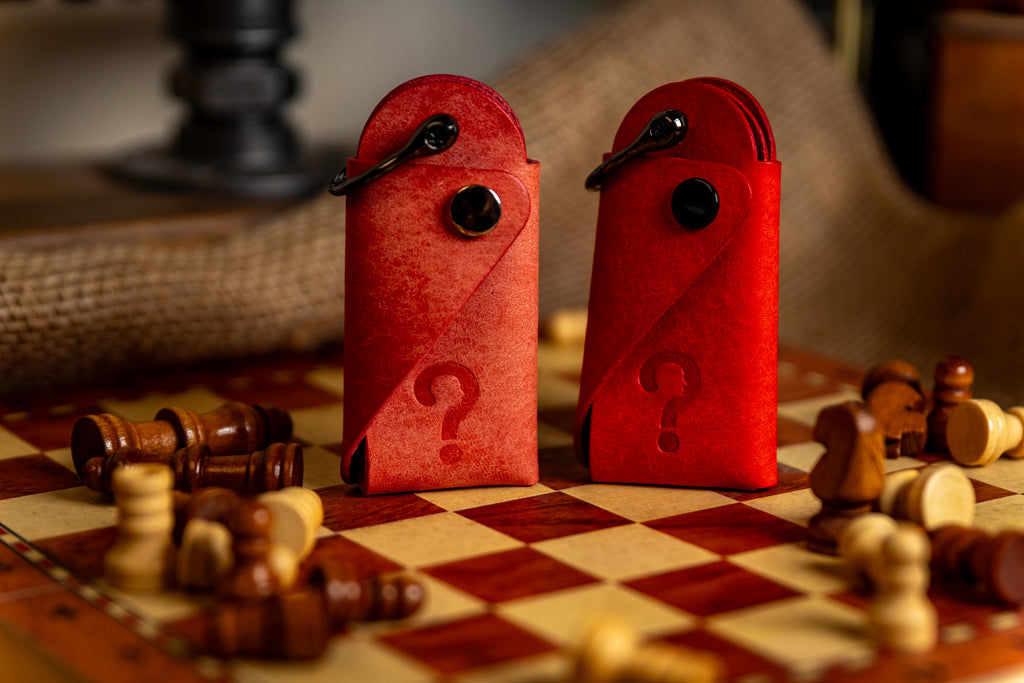 Red and Pink leather key cases with question marks on a chessboard with chess pieces.