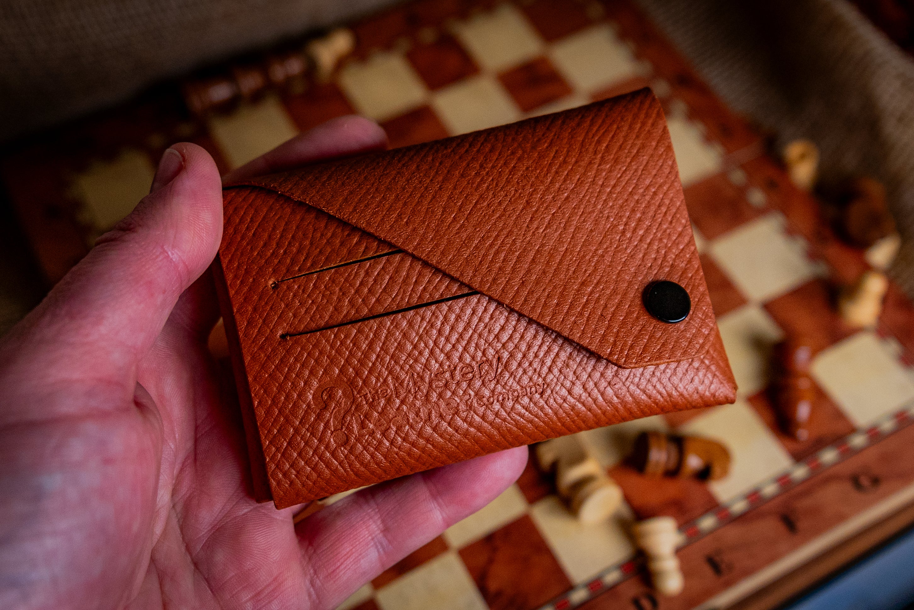 Brown leather cardholder held in a hand with a checkered background