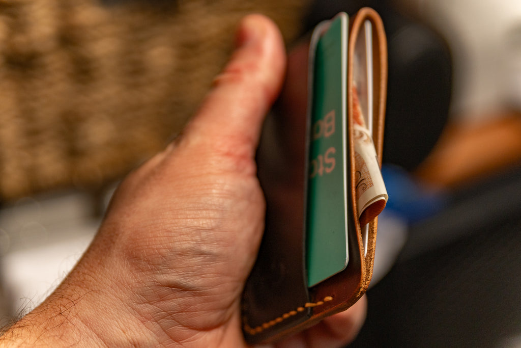 Hand holding a leather wallet with a card and money clip.