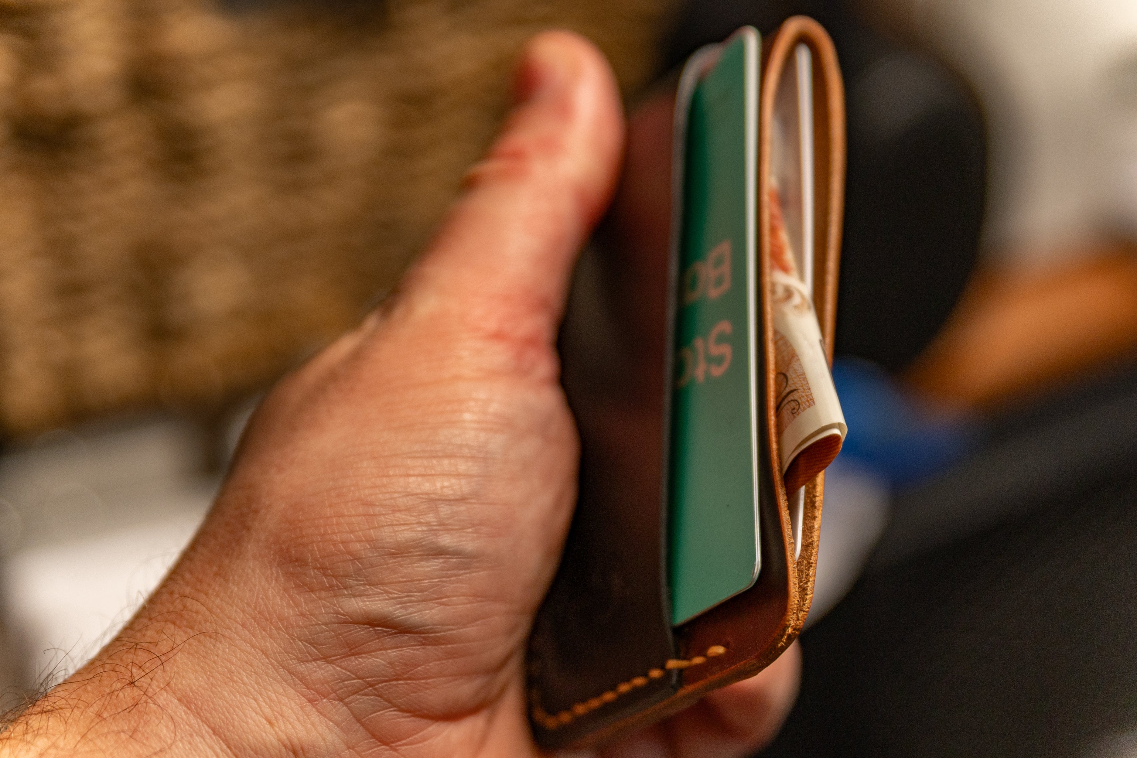 Hand holding a leather wallet with a card and money clip.