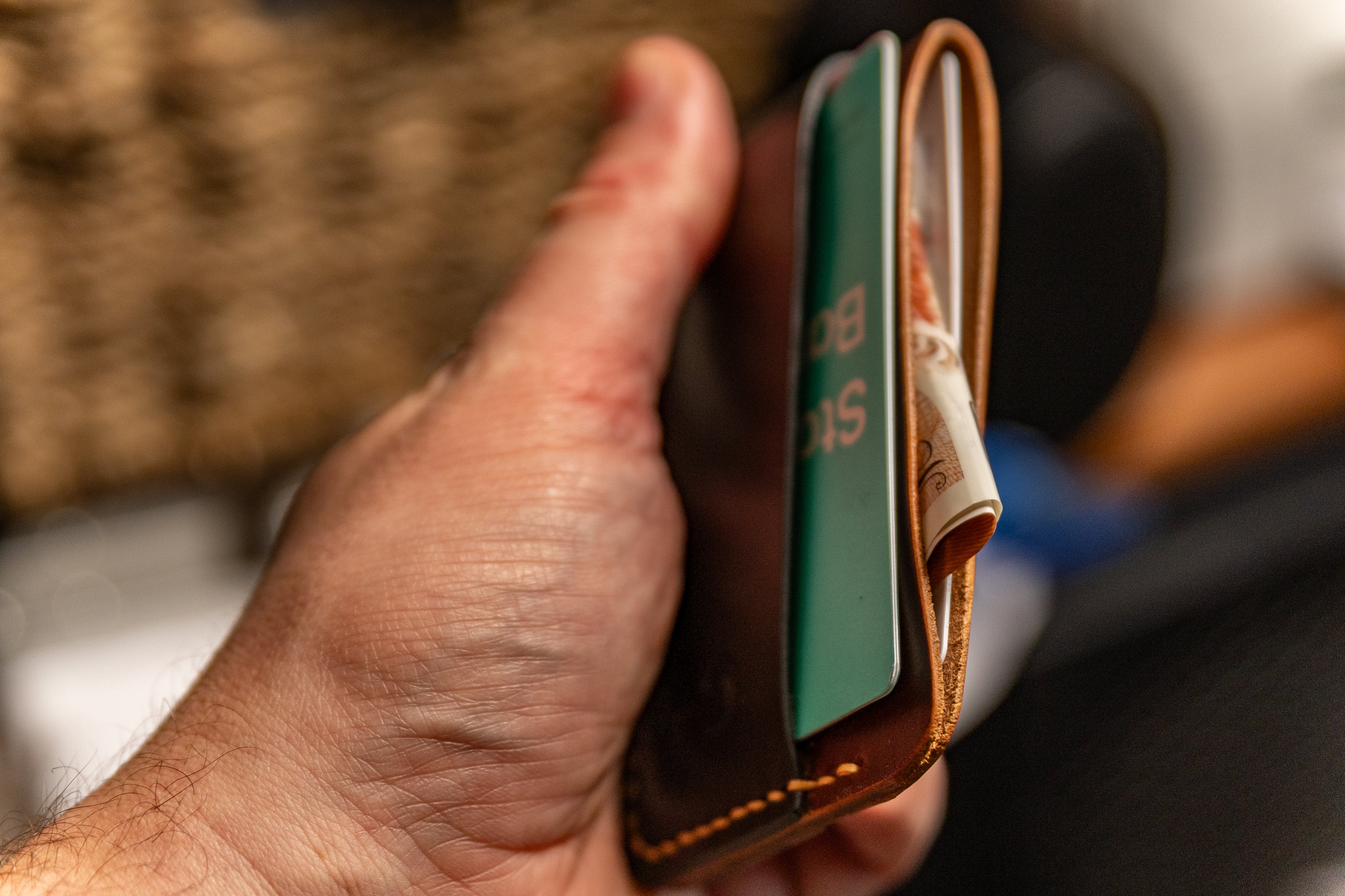 Hand holding a leather wallet with a card and money clip.