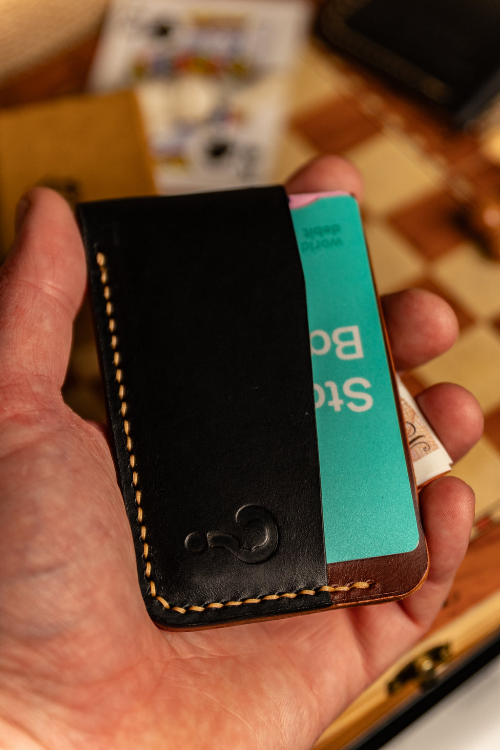 Hand holding a black leather cardholder with a turquoise card inside, on a blurred background.