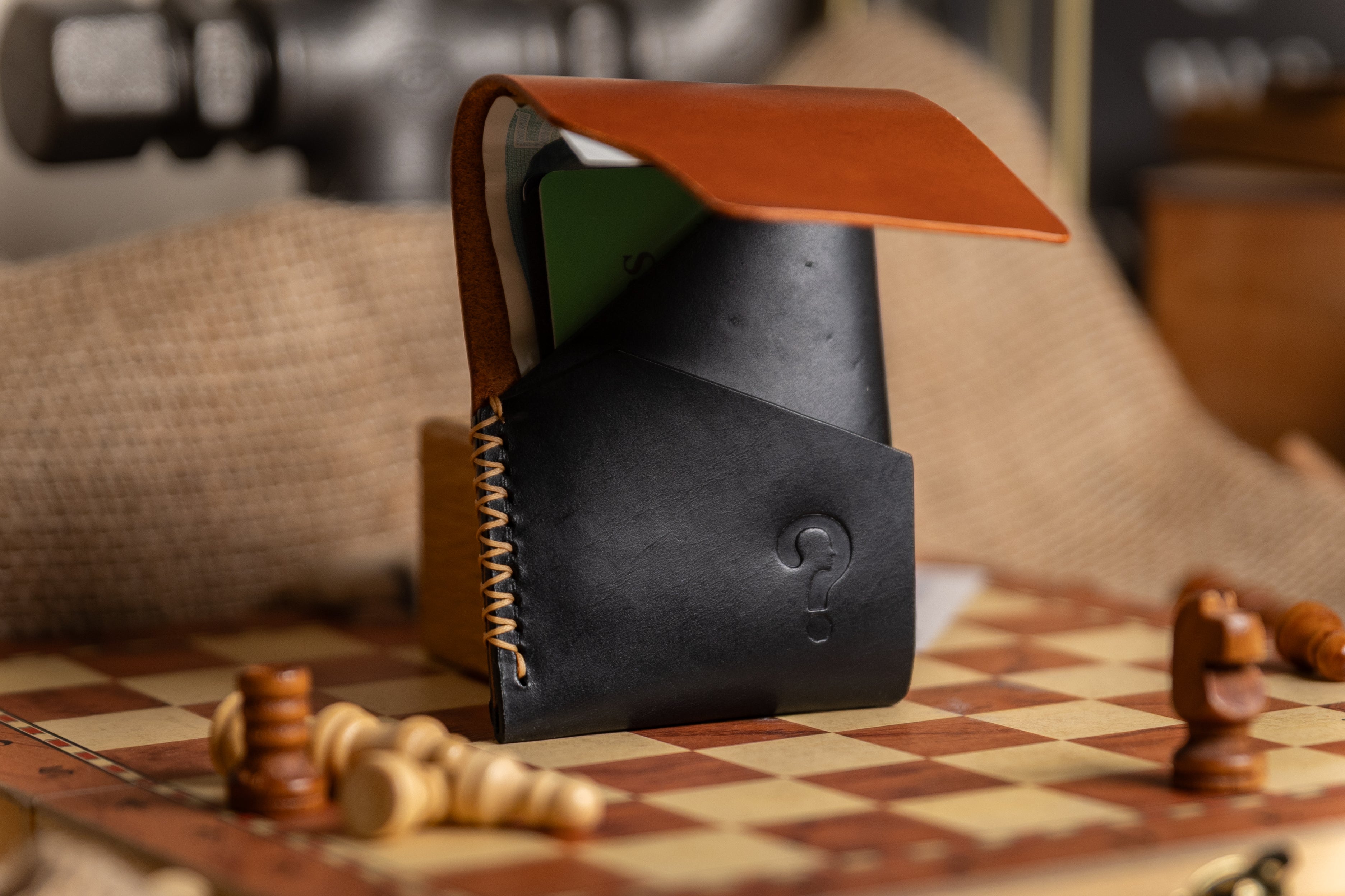 Black leather wallet with brown flap on a checkered surface with chess pieces