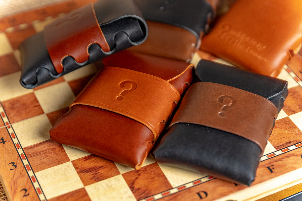 Three buttero walpier leather pouches in brown, black, and brown with a question mark on a chessboard.