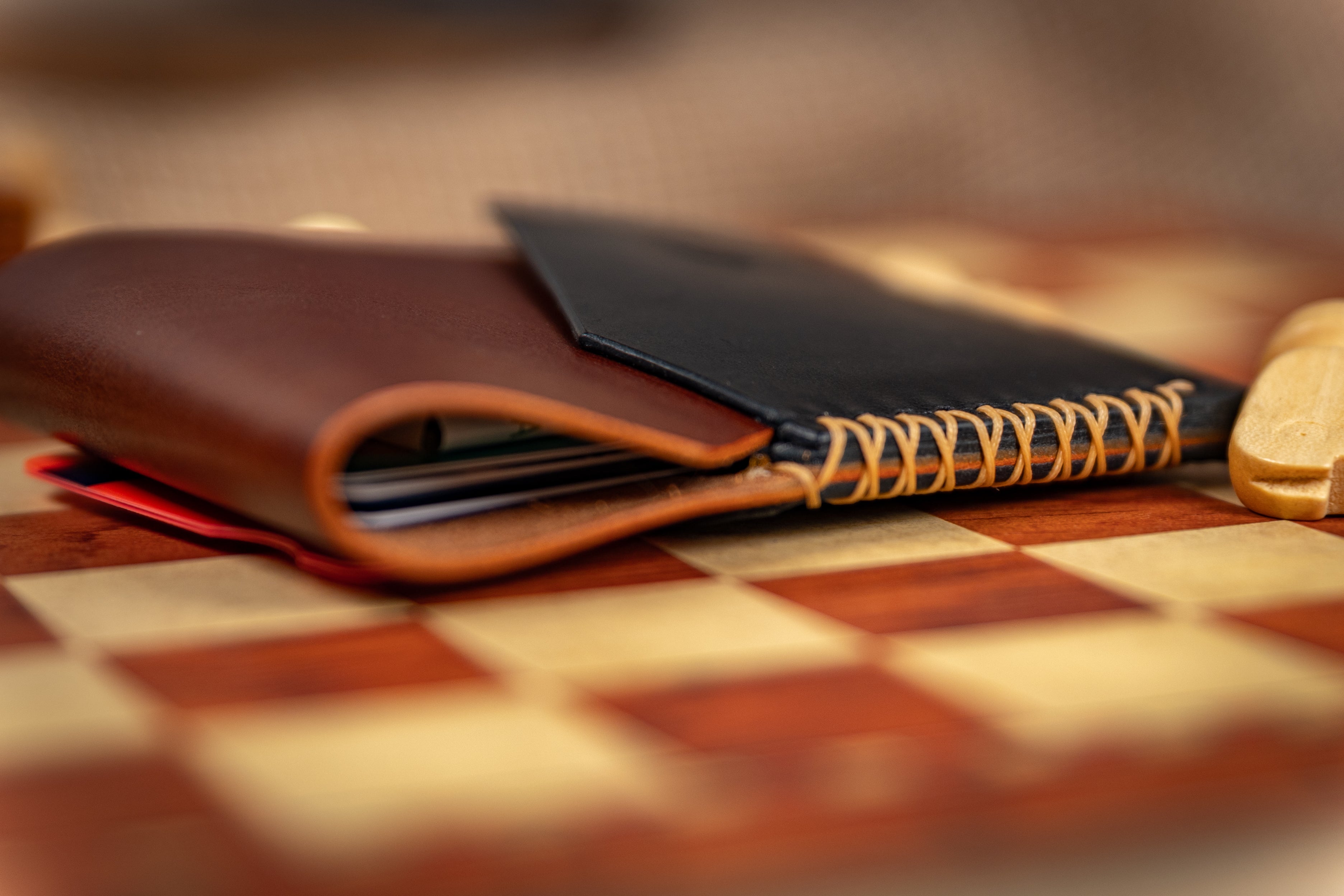 Brown leather wallet and black notebook on a checkered tablecloth