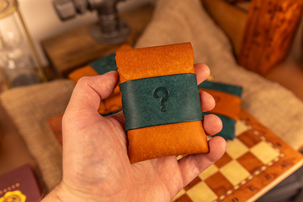 Hand holding a small pueblo leather wallet with a question mark design on a checkered surface.