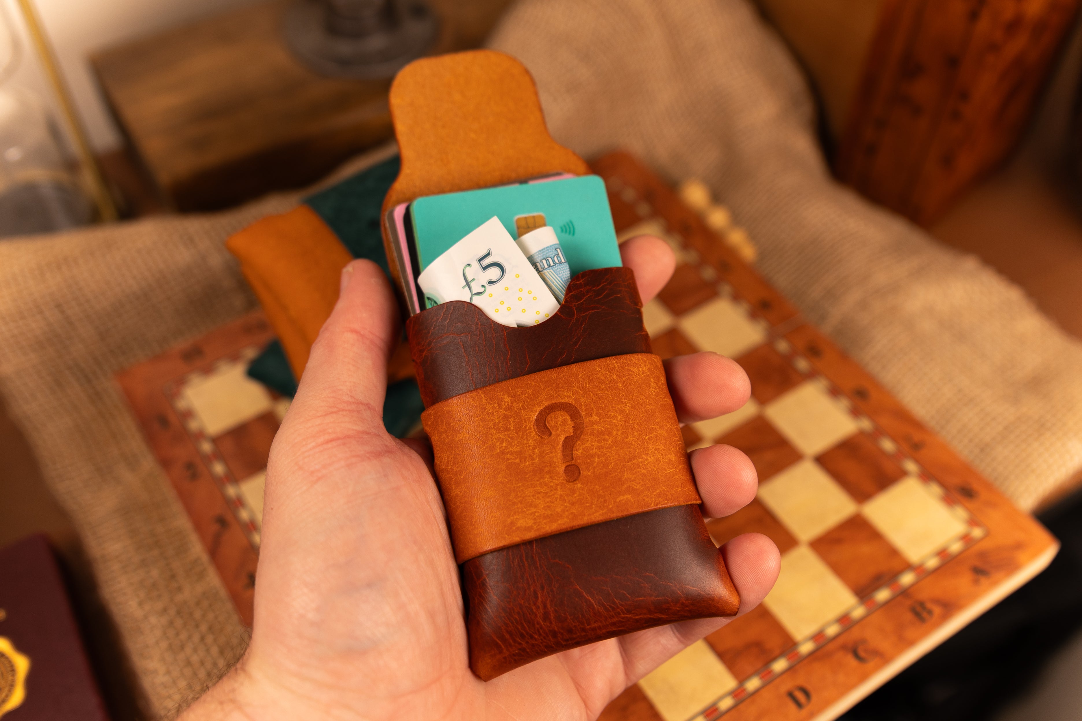 Hand holding a brown leather wallet with cards against a blurred indoor background