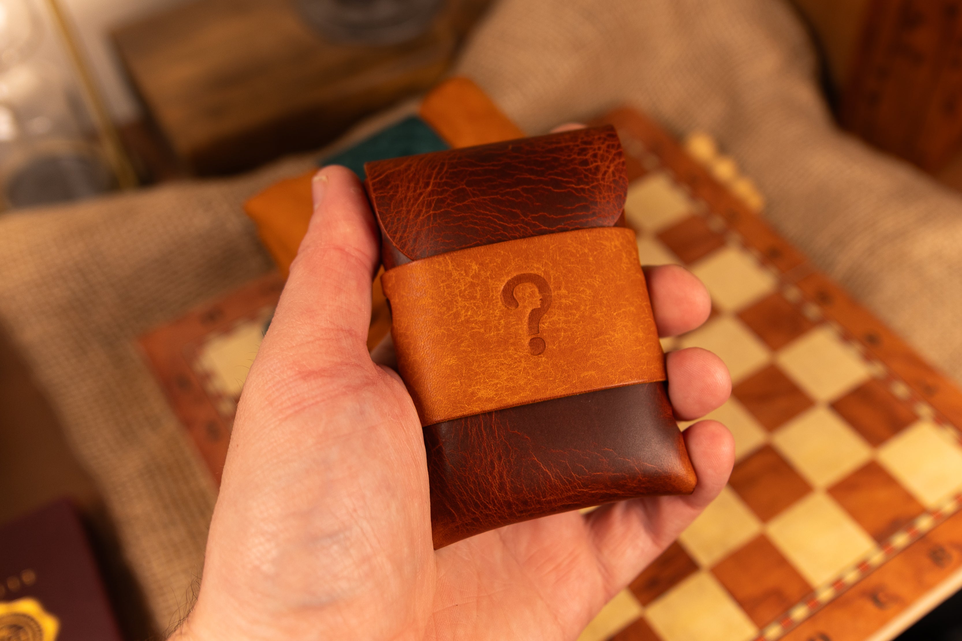 Hand holding a brown leather wallet with a question mark emblem on a checkered surface.