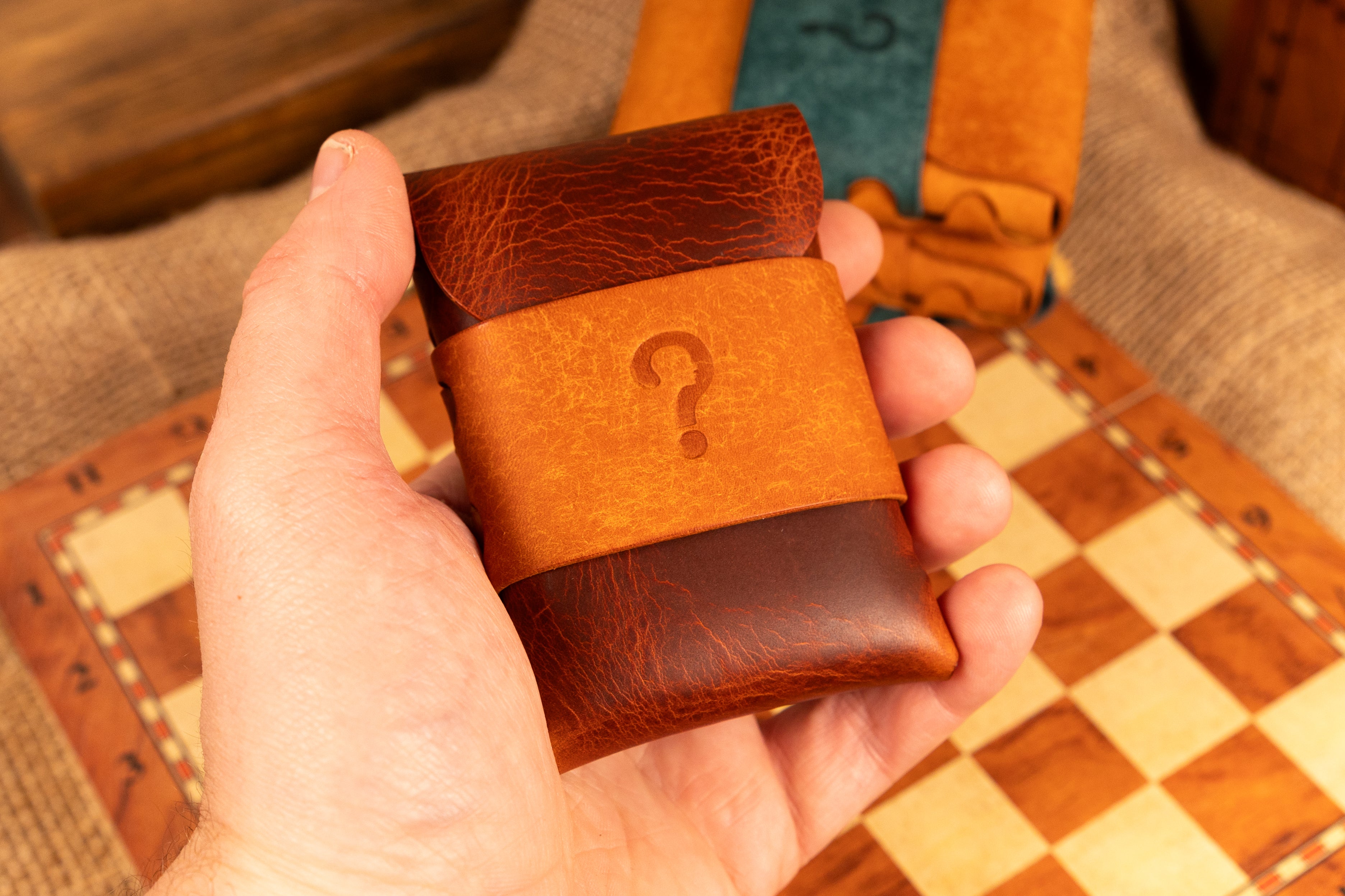 Hand holding a brown leather wallet with a question mark on a checkered surface