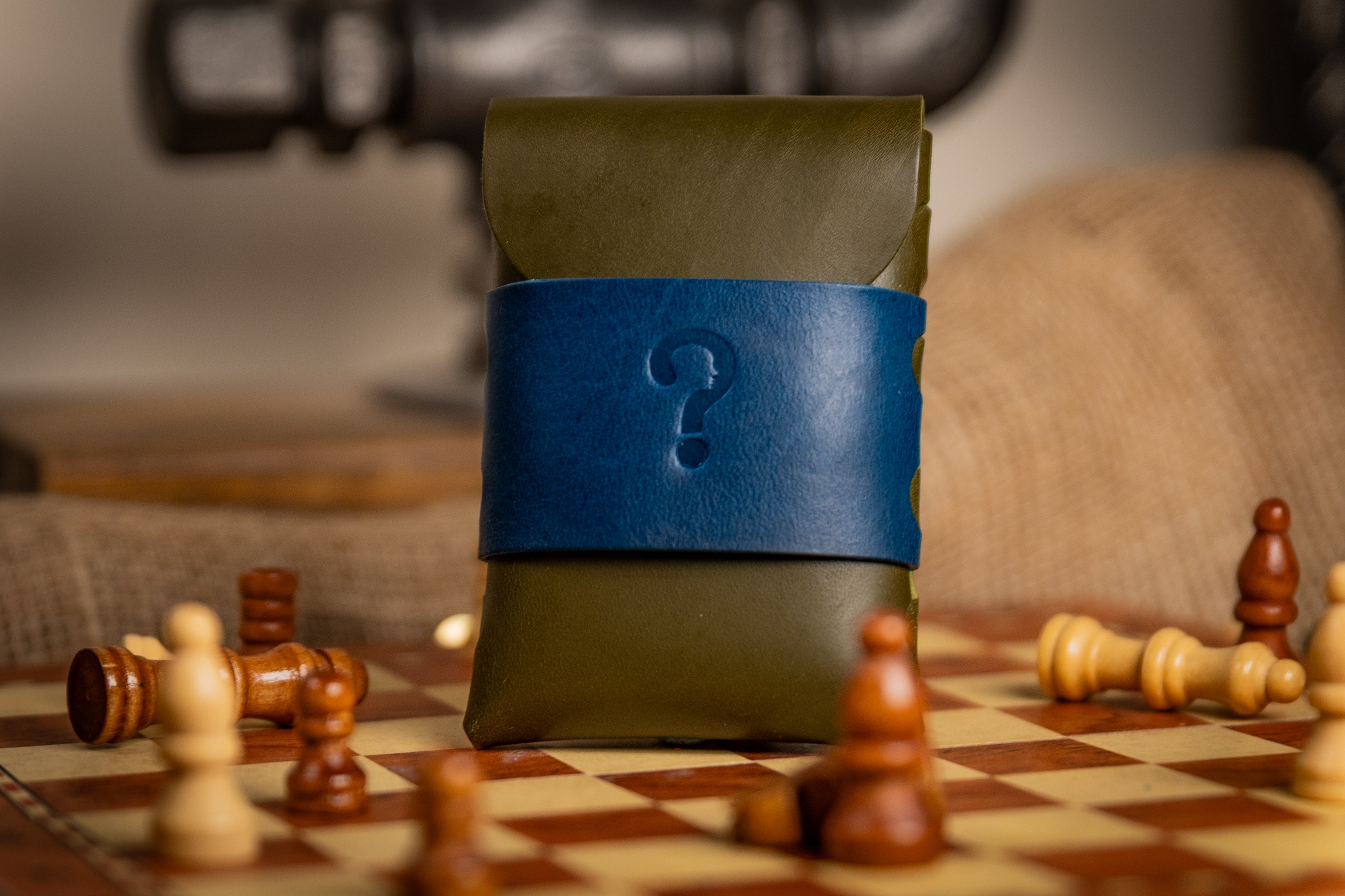 Green walpier buttero leather wallet with a blue strap featuring a question mark on a chessboard with wooden chess pieces.