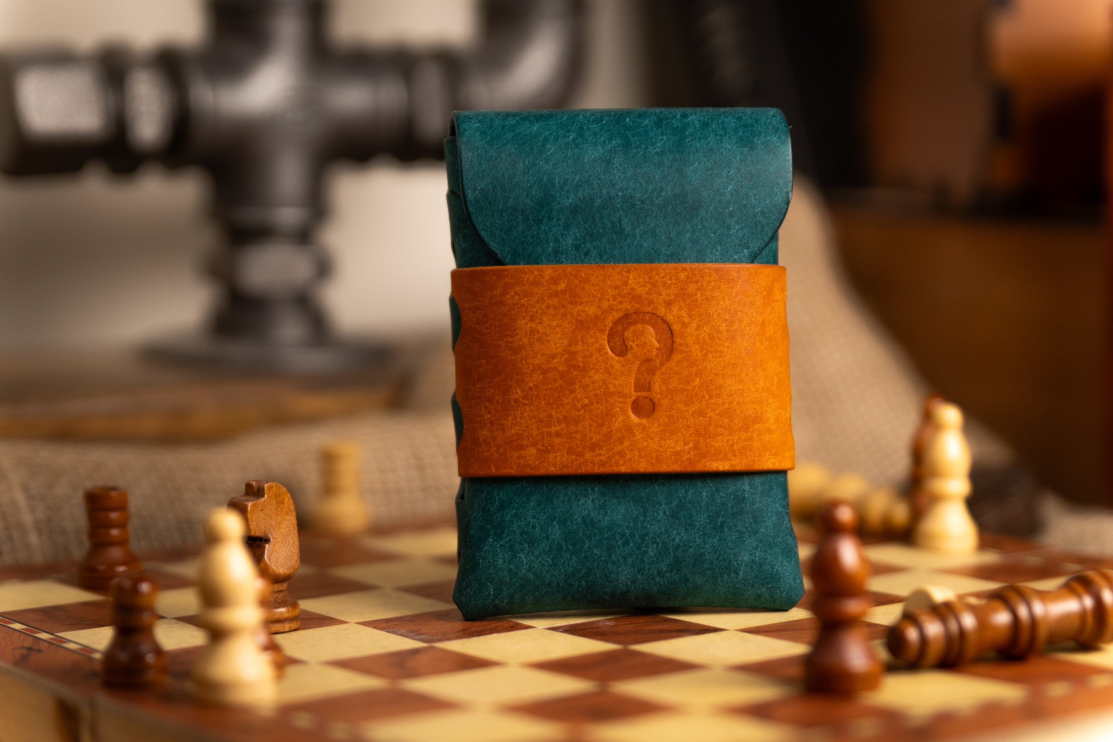 Teal pueblo leather wallet pouch with a brown strap featuring a question mark on a chessboard.
