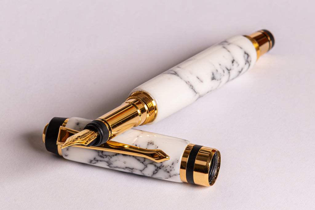 A luxury fountain pen with a white and gray marble-patterned resin body and polished gold-tone metal accents, shown on a clean light gray background.