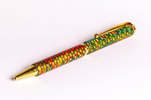 A decorative ballpoint pen with a vibrant, multicolored marbled pattern in green, yellow, red, and orange, accented with shiny gold metal trim, clip, and tip, set against a plain white background.