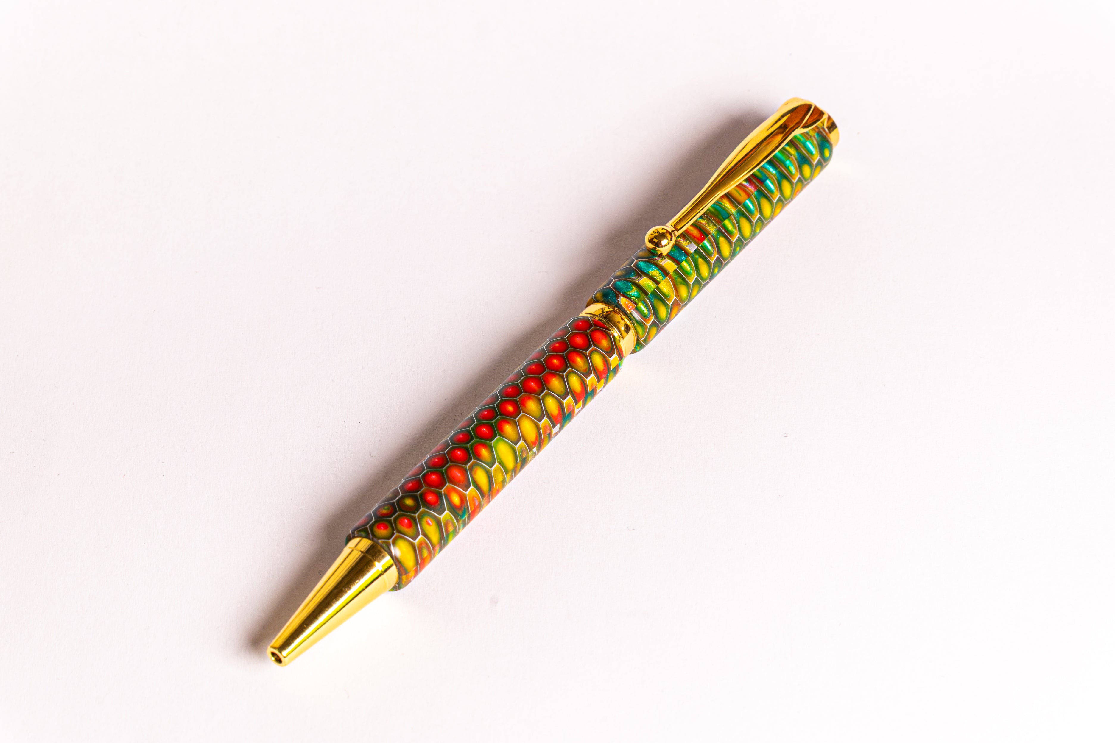 A gold-plated ballpoint pen with a vibrant, multicolored marbled pattern in red, green, yellow, and blue, shown diagonally on a plain white background.