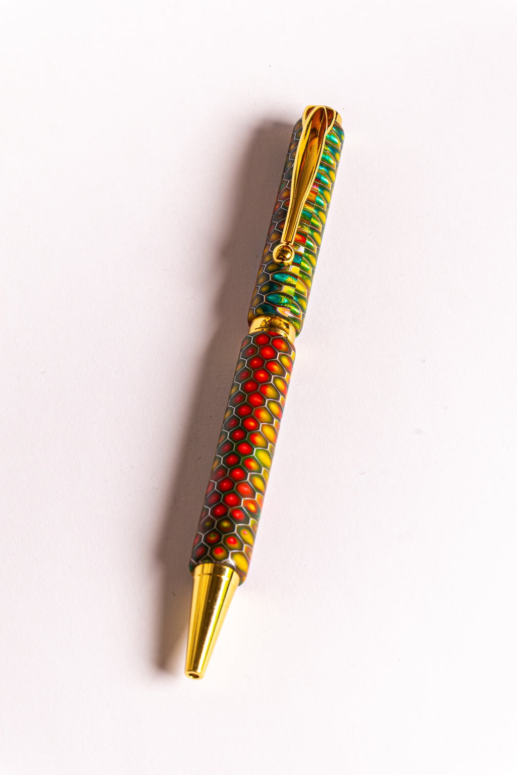 A decorative ballpoint pen with a gold-tone clip and tip, featuring a colorful patterned barrel with red, green, yellow, and black dots on a white background.